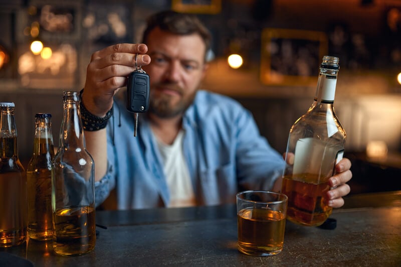 a man holding alcohol and keys deciding whether or not to drive