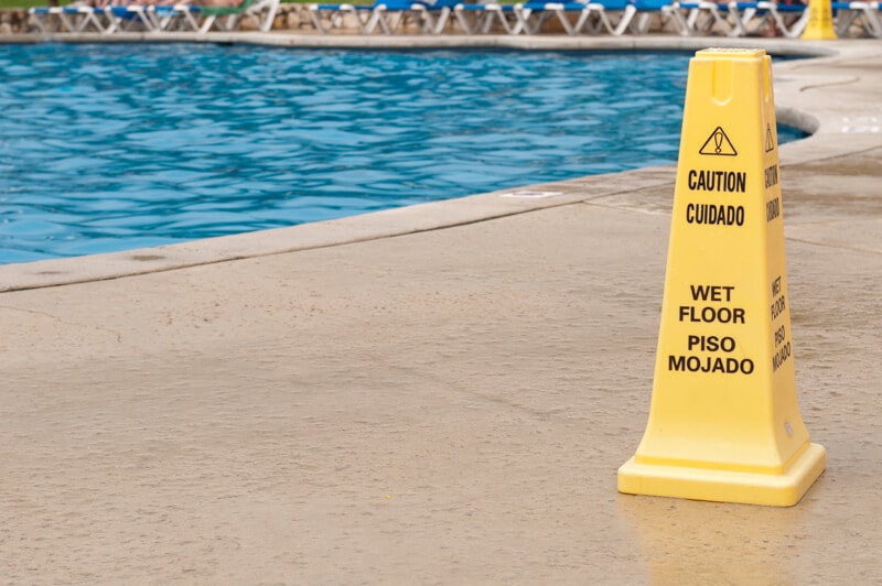the side of a swimming pool with a yellow sign that says caution wet floor in English and Spanish
