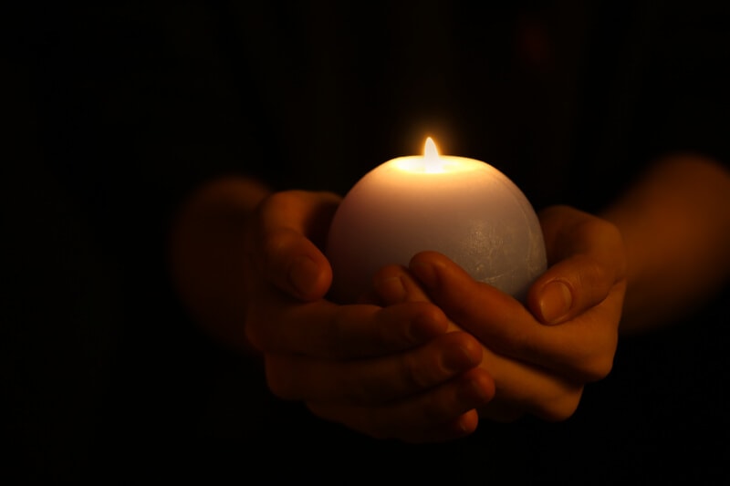 a person's hands holding a lit candle in a dark area